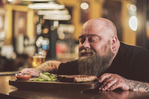 Ein Mann mit Vollbart riecht mit geschlossenen Augen an einem Steak