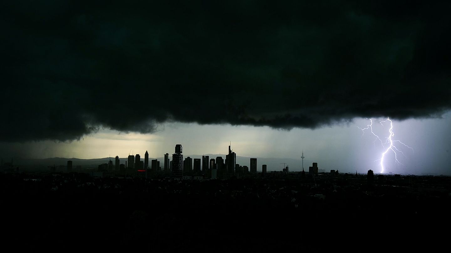 Tiefschwarze Gewitterwolken über einem Stadtpanorama, rechts ist ein Blitz zu sehen