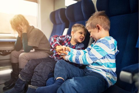 Eine Mutter fährt mit zwei Kindern Zug, die sich streiten. Sie guckt verzweifelt