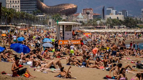 Besucher liegen auf Handtüchern am Strand von Barcelona