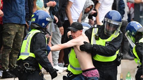 Zwei Polizisten mit Helmen und Schutzkleidung versuchen, einen jungen, weißen Mann mit nacktem Oberkörper festzuhalten