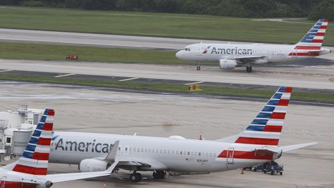 Zwei Flieger von American Airlines, einer steht, einer landet im Hintergrund auf dem Flughafen
