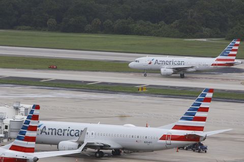 Zwei Flieger von American Airlines, einer steht, einer landet im Hintergrund auf dem Flughafen