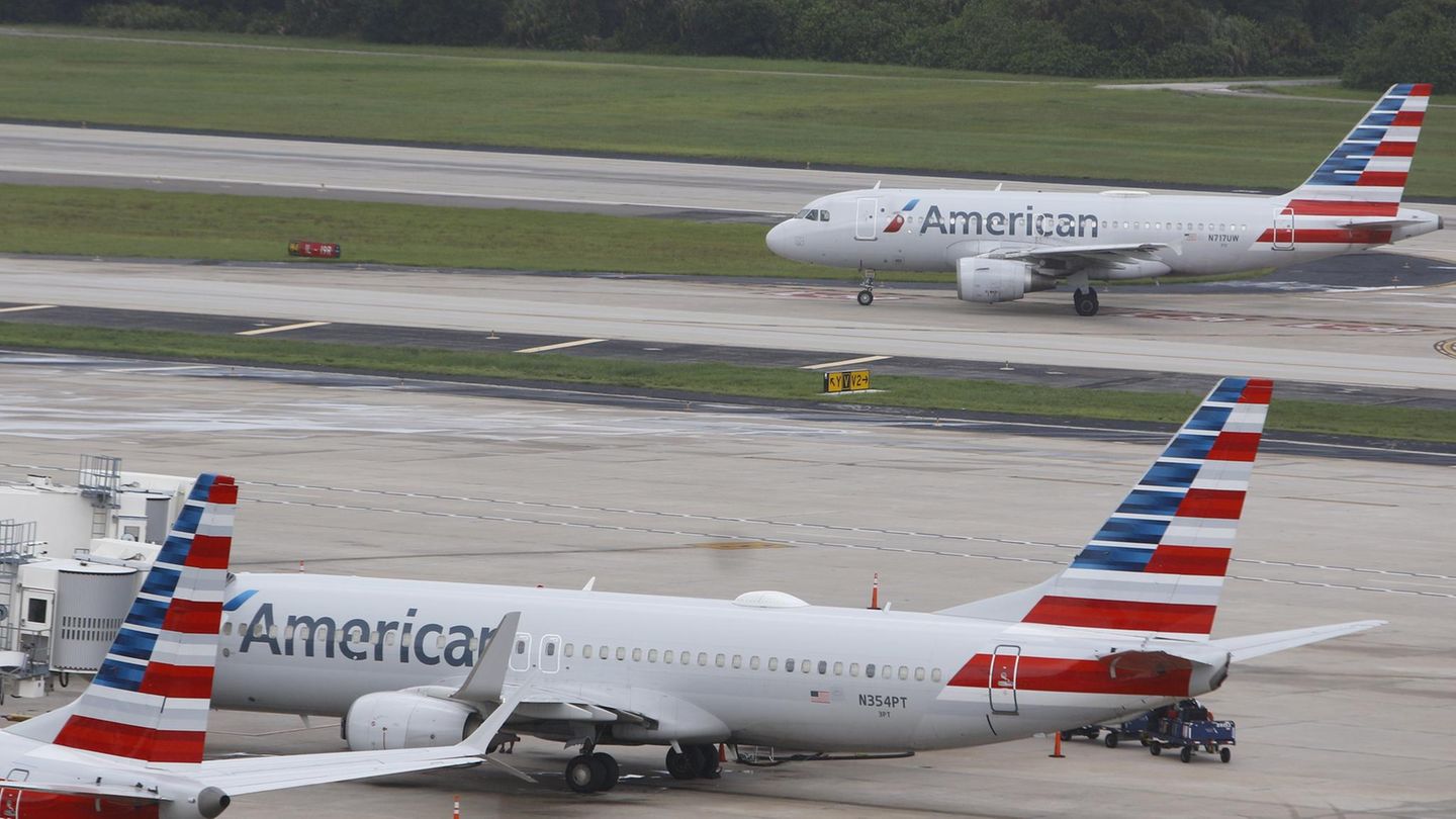 Zwei Flieger von American Airlines, einer steht, einer landet im Hintergrund auf dem Flughafen