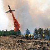Feuerwehrleute beobachten und filmen mit ihren Handys, wie ein Flugzeug Löschmittel abwirft