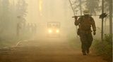 Ein Alaska Smokejumper und andere Feuerwehrleute gehen auf eine Straße hinter dem Chena Hot Springs Resort. Günstige Wetterbedingungen haben es den Feuerwehrleuten ermöglicht, den Schutz vor einem Waldbrand im Inneren Alaskas zu verstärken, auch wenn das Feuer auf der gegenüberliegenden Seite größer wird. 