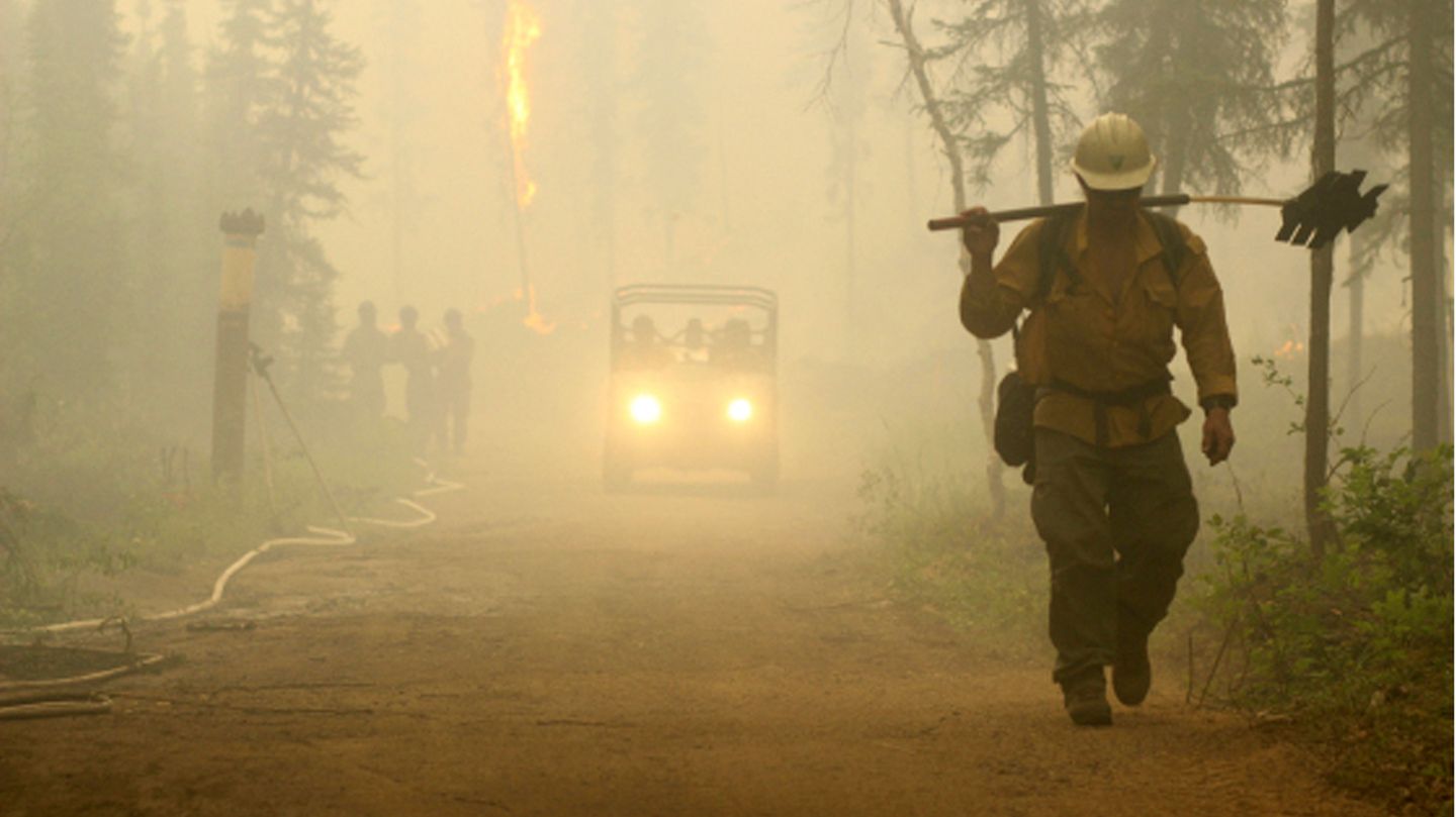 Geschafft Ein Alaska Smokejumper und andere Feuerwehrleute gehen auf eine Straße hinter dem Chena Hot Springs Resort. Günstige Wetterbedingungen haben es den Feuerwehrleuten ermöglicht, den Schutz vor einem Waldbrand im Inneren Alaskas zu verstärken, auch wenn das Feuer auf der gegenüberliegenden Seite größer wird.