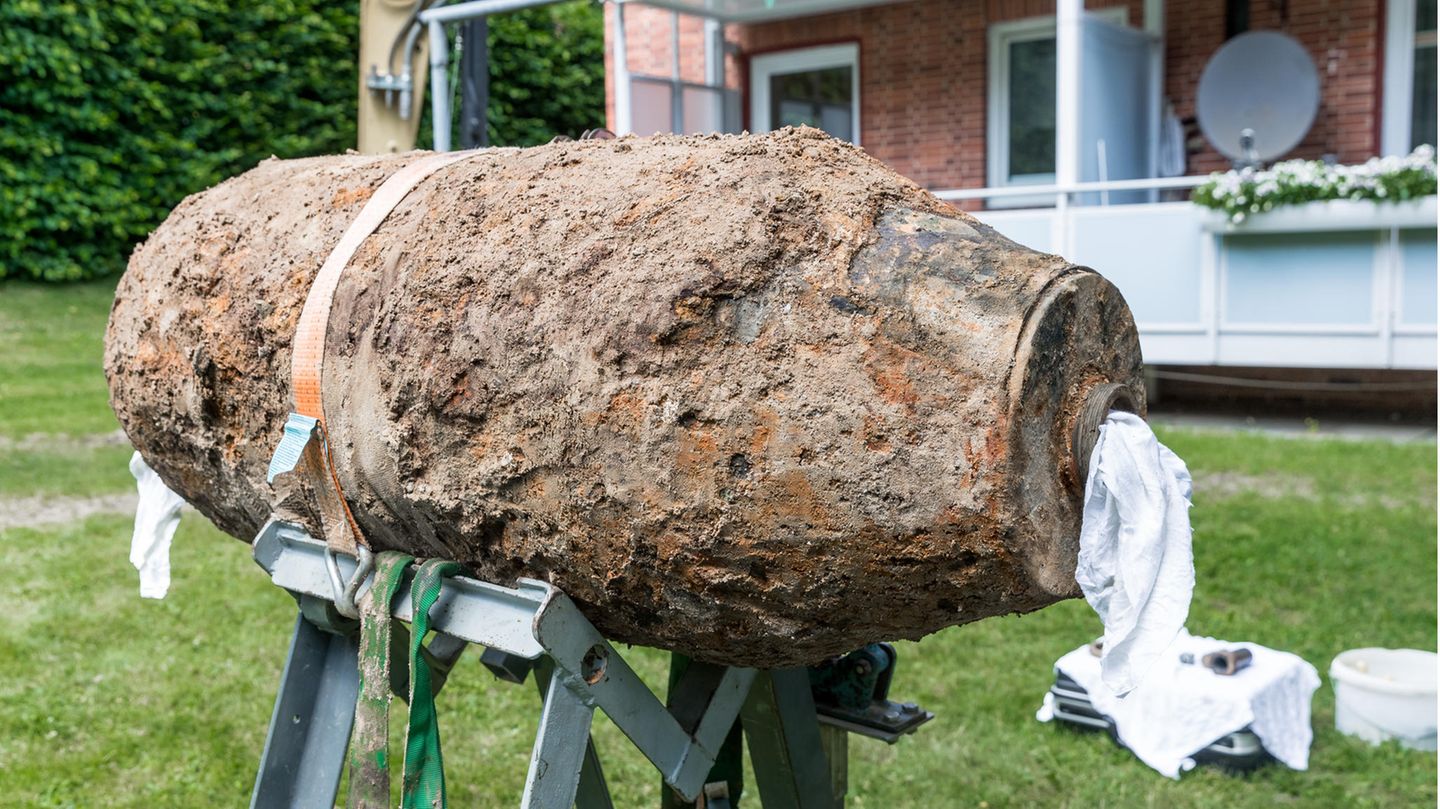 Eine mit Erde und Rost überzogene Bombe liegt auf einem Gestell vor einem Mehrfamilienhaus