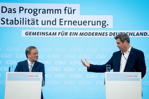 Auf einer Bühne mit hellblauem Hintergrund stehen zwei Rednerpulter, an denen zwei weiße Männer in Anzügen stehen