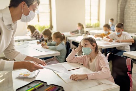 Schülerin mit Gesichtsmaske im Gespräch mit einem Lehrer
