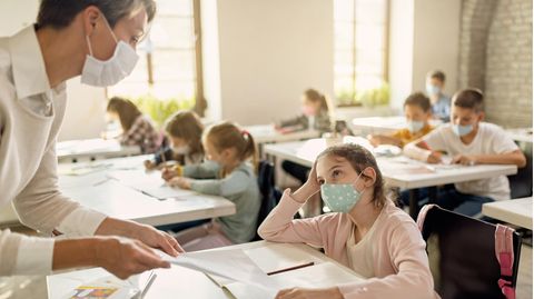 Schülerin mit Gesichtsmaske im Gespräch mit einem Lehrer