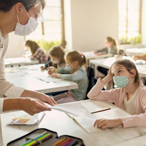 Schülerin mit Gesichtsmaske im Gespräch mit einem Lehrer