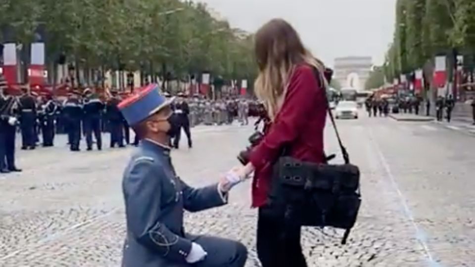 Mitten auf den Champs-èlysées kniet ein Soldat in Gardeuniform vor seiner blonden Freundin, die steht