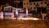 Drei Personen machen Fotos und beobachten die Wassermassen, die sich über eine Straße und ein Restaurant ausbreiten
