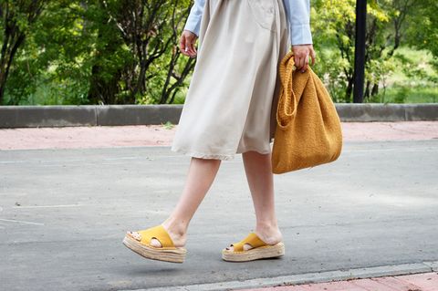 Frau im Kleid hat Sandalen in der Hand