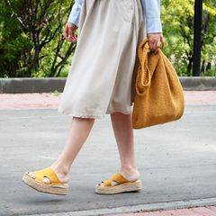 Frau im Kleid hat Sandalen in der Hand