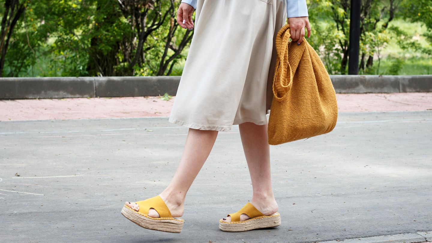 Frau im Kleid hat Sandalen in der Hand