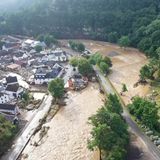 Auf einer Luftaufnahme ist ein Ort zu sehen, um den sich ein Hochwasser führender brauner Fluss windet