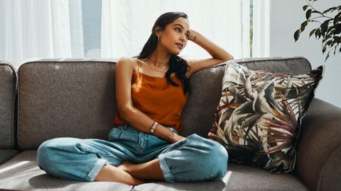 Frau sitzt auf dem Sofa und guckt verträumt zur Seite.