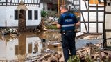 Ein Polizist in blauer Uniform und Warnweste steht auf einem Schutthaufen und schaut über Wasserflächen und Trümmer