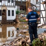 Ein Polizist in blauer Uniform und Warnweste steht auf einem Schutthaufen und schaut über Wasserflächen und Trümmer
