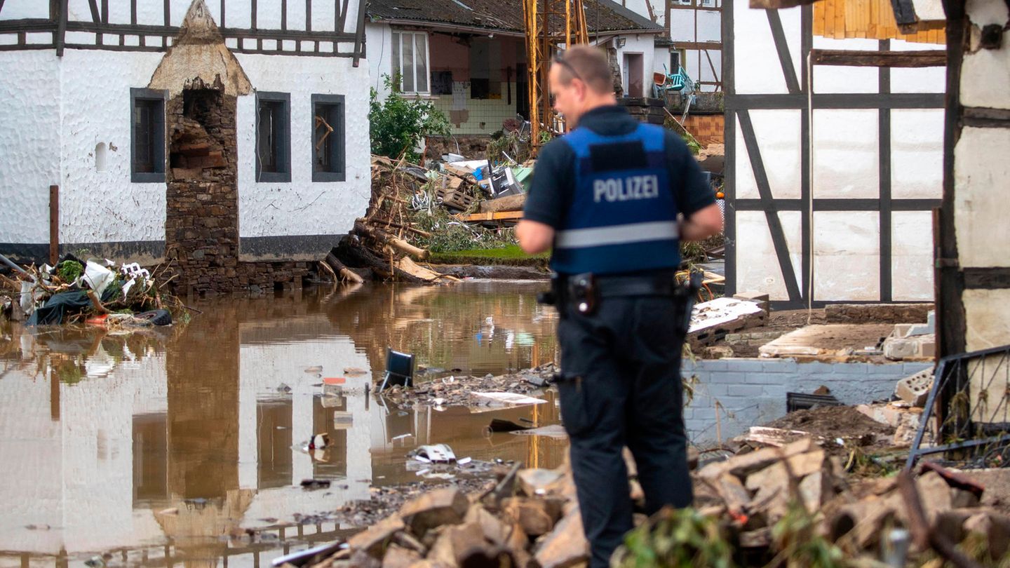 Ein Polizist in blauer Uniform und Warnweste steht auf einem Schutthaufen und schaut über Wasserflächen und Trümmer