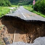 In einer Straße zwischen Büschen und Wiesen ist die Fahrbahn auf voller Breite weggebrochen und in eine Unterspülung gestürzt