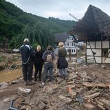 Zwei Erwachsenen und drei Kinder stehen am Ufer eines Flusslaufes inmitten von Schlamm und Trümmern.