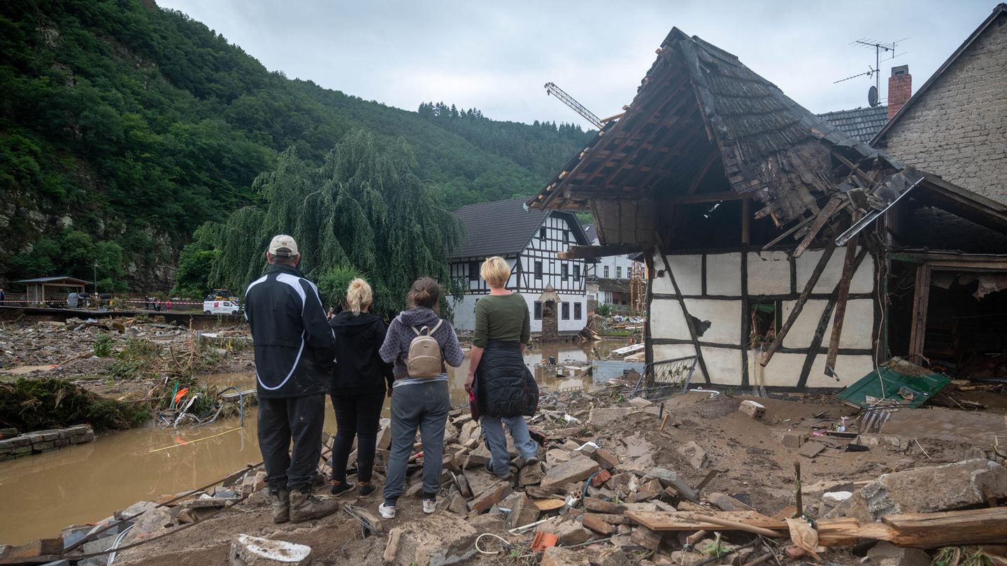 Zwei Erwachsenen und drei Kinder stehen am Ufer eines Flusslaufes inmitten von Schlamm und Trümmern.