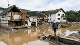 Ein Mann in Gummistiefeln und Arbeitshose geht auf einem Mäuerchen auf ein vom Wasser zerstörtes Fachwerkhaus zu