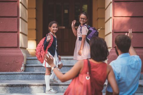 Kinder verabschieden sich winkend von ihren Eltern und gehen in die Schule