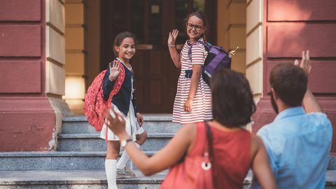 Kinder verabschieden sich winkend von ihren Eltern und gehen in die Schule