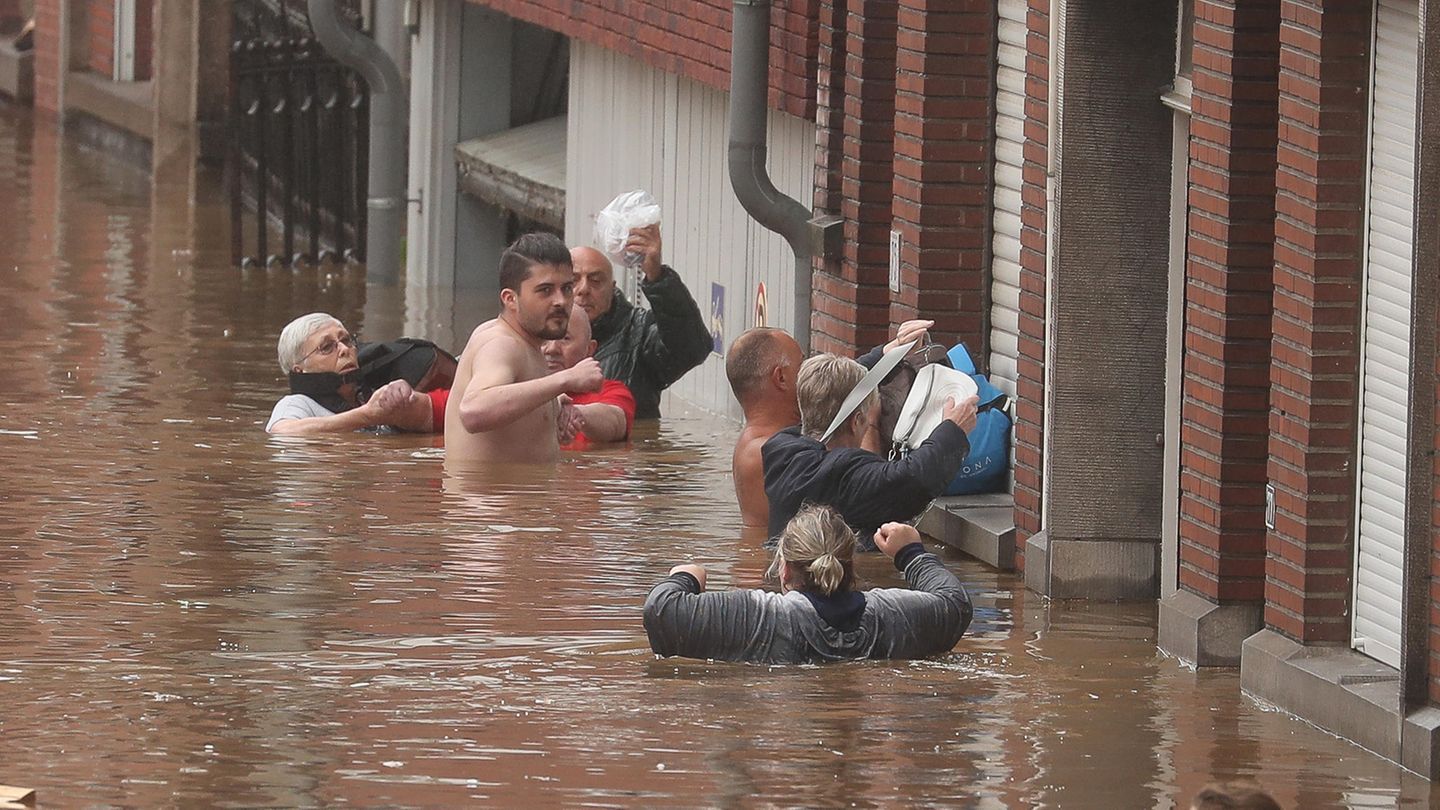 Sechs Menschen stehen teils bis unter die Achseln im Hoochwasser und versuchen, ihre Habseligkeiten trocken zu halten