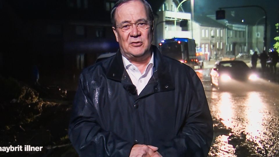 Armin Laschet in der Zuschalte bei Illner, er steht im Regenmantel vor einer verregneten Straße