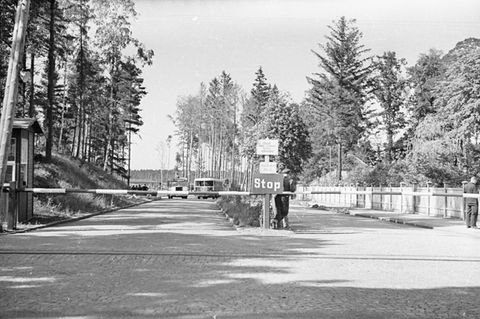 Ein Schwarzweiß-Foto zeigt die Einfahrt zum ehemaligen KZ Stutthof mit einem Stoppschild davor