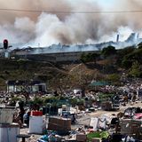 Spuren der Gewalt in Durban: Rauch steigt aus einer Fabrik im Hintergrund auf, während leere Kisten von geplünderten Waren auf einer Fahrbahn liegen.