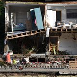 Ein Mann schiebt eine Schubkarre an einem zerstörten Haus vorbei