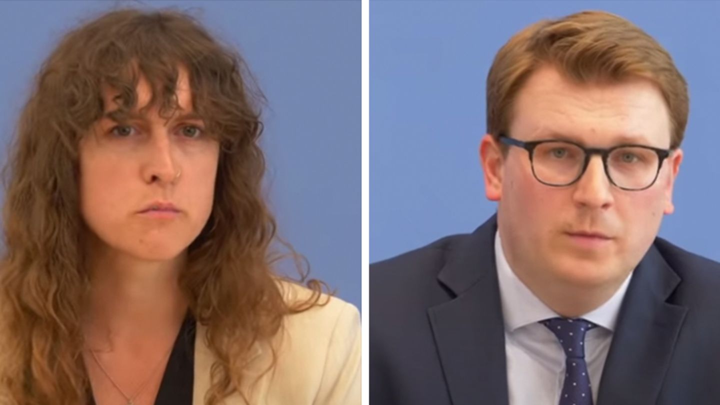 Eine weiße Frau mit halblangen, braunen Locken und ein weißer Mann mit schwarzer Brille und blondem Seitenscheitel sitzen