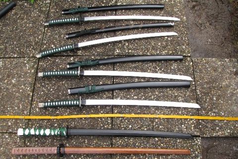 Neben einem gelben Gleidermaßstab liegen Samurai-Schwerter aufgereiht auf einem Boden aus Waschbeton-Platten