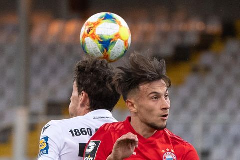 Zwei Fußballer - einer ganz in Rot, einer in Weiß und Dunkelblau – steigen Rücken an Rücken zum Kopfball hoch