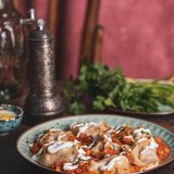 Mantu (gedämpfte Teigtaschen mit Hackfleisch)      Zutaten:   Für den Teig: 250 g Weizenmehl Type 405 plus etwas mehr nach Bedarf, 1 Päckchen Trockenhefe, 1 TL Salz  Für die Füllung: Pflanzenöl zum Anbraten, 500 g Rinder- und/oder Lammhackfleisch, Salz, frisch gemahlener schwarzer Pfeffer, 1 Tomate, 2 Zwiebeln  Für die Kichererbsensauce: 1 Tomate, 1 Zwiebel, 50 g getrocknete gespaltene Kichererbsen (Daal Chana; in orientalischen oder asiatischen Supermärkten erhältlich), Pflanzenöl zum Anbraten, 1 TL Paprikapulver, 1 TL Korianderpulver, Salz, frisch gemahlener schwarzer Pfeffer  Für die Joghurtsauce: 2 Knoblauchzehen, 500 g Naturjoghurt, Salz  Außerdem: 3 TL getrocknete Minze (oder gehackter frischer Koriander)      Zubereitung:  1. Für den Teig das Mehl, die Hefe, das Salz und 150 ml lauwarmes Wasser zu einem Teig verkneten. Wenn er zu klebrig ist, noch etwas Mehl dazugeben. Den Teig abgedeckt 30 Minuten ruhen lassen.  2. Inzwischen für die Füllung Öl in einer Pfanne erhitzen und das Hackfleisch darin braun anbraten. Anschließend mit Salz und Pfeffer würzen. Die Tomate waschen und den Stielansatz herausschneiden. Die Zwiebeln abziehen. Beides in Würfel schneiden. Die Tomate zum Hackfleisch geben und so lange mitschmoren, bis die Flüssigkeit verdampft ist. Dann die Zwiebeln zufügen und alles noch etwas weiterschmoren lassen.  3. Für die Kichererbsensauce die Tomate waschen und den Stielansatz herausschneiden. Die Zwiebel abziehen. Beides in Würfel schneiden. Die Kichererbsen unter fließendem Wasser abspülen, bis das abfließende Wasser klar bleibt. Öl in einer tiefen Pfanne erhitzen und die Zwiebel darin goldbraun anbraten. Anschließend die Kichererbsen und die Tomaten dazugeben. So viel Wasser angießen, dass die Kichererbsen komplett damit bedeckt sind. Aufkochen und 10 Minuten kochen lassen, bis die Kichererbsen weich sind. Zuletzt die Sauce mit dem Paprikapulver, dem Korianderpulver, Salz und Pfeffer würzen.  4. Für die Joghurtsauce den Knoblauch abziehen und pressen. Dann mit dem Joghurt verrühren. Die Sauce dezent mit Salz abschmecken.  5. Den Teig sehr dünn ausrollen und in 5 x 5 cm große Vierecke schneiden. Die Füllung mittig auf die Teigstücke geben und die Teigecken leicht mit Wasser einpinseln. Die Ecken nach oben ziehen und oben sowie seitlich so zusammendrücken, dass Säckchen entstehen  6. Wasser in einem Topf aufkochen. Die Teigtaschen in einen Dampfeinsatz setzen und mit geschlossenem Deckel im Wasserdampf etwa 30 Minuten dämpfen; sie dürfen dabei das Wasser nicht berühren. Alternativ lassen sie sich auch in einem Dampfgartopf garen.  7. Zum Anrichten etwas Joghurtsauce auf einen Teller geben, die Teigtaschen darauflegen und mit der restlichen Joghurtsauce übergießen. Zum Schluss die Kichererbsensauce darüber verteilen. Die Mantu mit der getrockneten Minze garnieren und servieren.