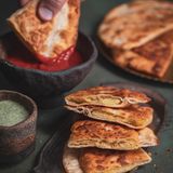 Bolani (Teigtaschen mit Kartoffelfüllung)      Zutaten:   Für den Teig: 500 g Weizenmehl Type 550 plus etwas mehr zum Arbeiten, 1 Päckchen Trockenhefe (ca. 9 g), 1 Prise Salz  Für die Füllung: 500 g vorwiegend festkochende Kartoffeln, Salz, Chilipulver, Korianderpulver, frisch gemahlener schwarzer Pfeffer, 1–2 EL Pflanzenöl  Außerdem: Pflanzenöl zum Frittieren (z. B. raffiniertes Olivenöl)      Zubereitung:  1. Für den Teig das Mehl, die Trockenhefe und das Salz in einer Schüssel mischen. In die Mitte der Mehl-Mischung eine Mulde drücken. 250 ml lauwarmes Wasser in die Mulde geben und die Zutaten mit den Händen in etwa 10 Minuten zu einem glatten, geschmeidigen Teig verkneten. Den Teig zu einer Kugel formen und mit einem feuchten Tuch abgedeckt etwa 2 Stunden gehen lassen, bis sich sein Volumen sichtbar vergrößert hat.  2. Für die Füllung die Kartoffeln gründlich abschrubben, waschen und in reichlich gesalzenem Wasser etwa 20 Minuten garen. Anschließend abgießen und ausdampfen lassen. Dann pellen und mit dem Kartoffelstampfer zerdrücken. Mit Chilipulver, Koriander, Salz und Pfeffer würzen. Zuletzt etwas Öl zufügen und alles gut vermengen.  3. Den aufgegangenen Teig auf der bemehlten Arbeitsfläche zu einer Rolle formen. Diese in zwölf Portionen teilen und daraus Kugeln formen. Die Kugeln auf der bemehlten Arbeitsfläche sehr dünn zu Kreisen ausrollen.  4. Die Kartoffel-Füllung portionsweise in die Mitte der Kreise geben. Die Teigränder mit Wasser bestreichen und jeweils eine Hälfte des Teiges über die Füllung klappen, sodass Halbmonde entstehen. Die Ränder gut mit den Zinken einer Gabel andrücken.  5. Öl etwa 4 cm hoch in eine Pfanne einfüllen und erhitzen. Die Teigtaschen portionsweise darin auf jeder Seite in etwa 2 Minuten goldbraun ausbacken, dabei zwischendurch wenden, damit sie gleichmäßig bräunen. Dann herausheben, auf Küchenpapier abtropfen lassen und beiseitestellen.  6. Warm servieren.