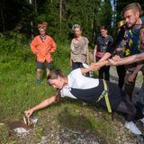  Alina versucht bei halb liegend eine Aufgabe zu erfüllen und wird dabei von den anderen Teilnehmern am Arm gehalten