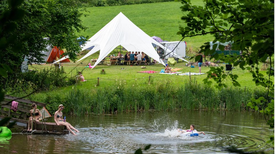 Bild 1 von 9 der Fotostrecke zum Klicken:  Teilnehmer eines Ferienlagers in Rosenberg in Baden-Württemberg schwimmen in einem See, während die anderen zusammen im Gemeinschaftszelt sitzen.