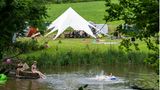 Bild 1 von 9 der Fotostrecke zum Klicken:  Teilnehmer eines Ferienlagers in Rosenberg in Baden-Württemberg schwimmen in einem See, während die anderen zusammen im Gemeinschaftszelt sitzen.