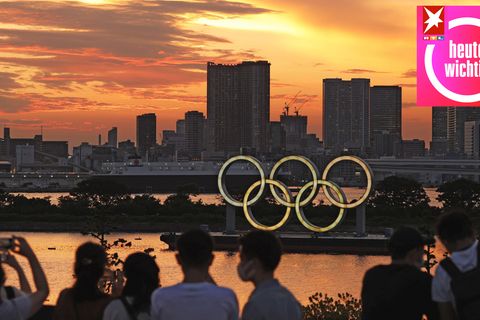Menschen schauen auf die bei Sonnenuntergang beleuchteten olympischen Ringe in der Bucht von Tokio