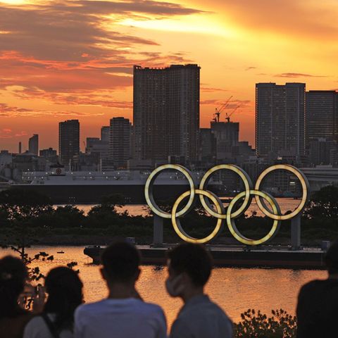 Menschen schauen auf die bei Sonnenuntergang beleuchteten olympischen Ringe in der Bucht von Tokio
