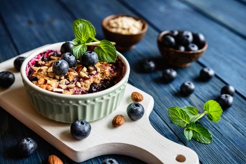 Eine Schale mit Baked Oatmeal mit Blaubeeren und Minze auf einem blauen Tisch