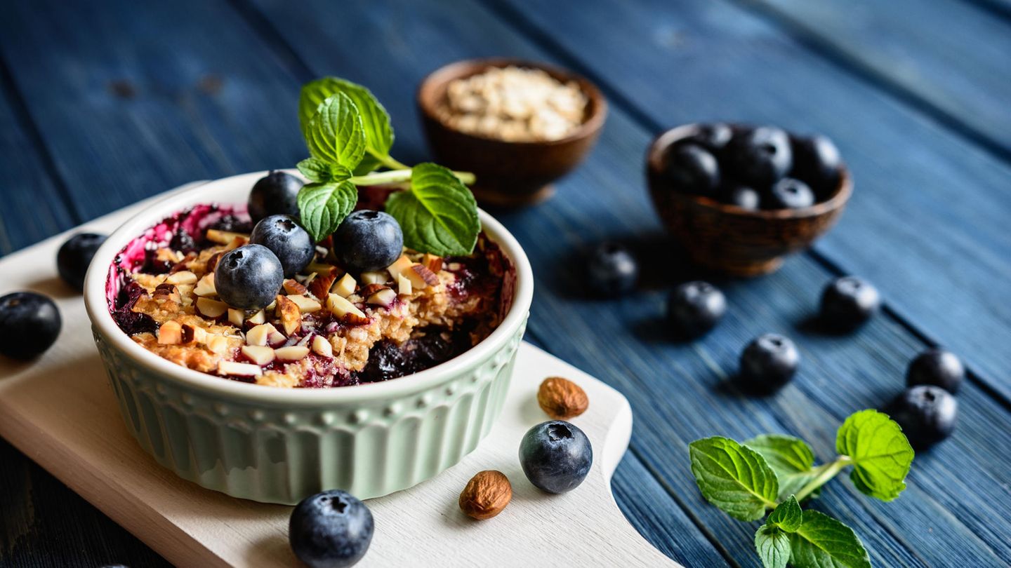 Eine Schale mit Baked Oatmeal mit Blaubeeren und Minze auf einem blauen Tisch
