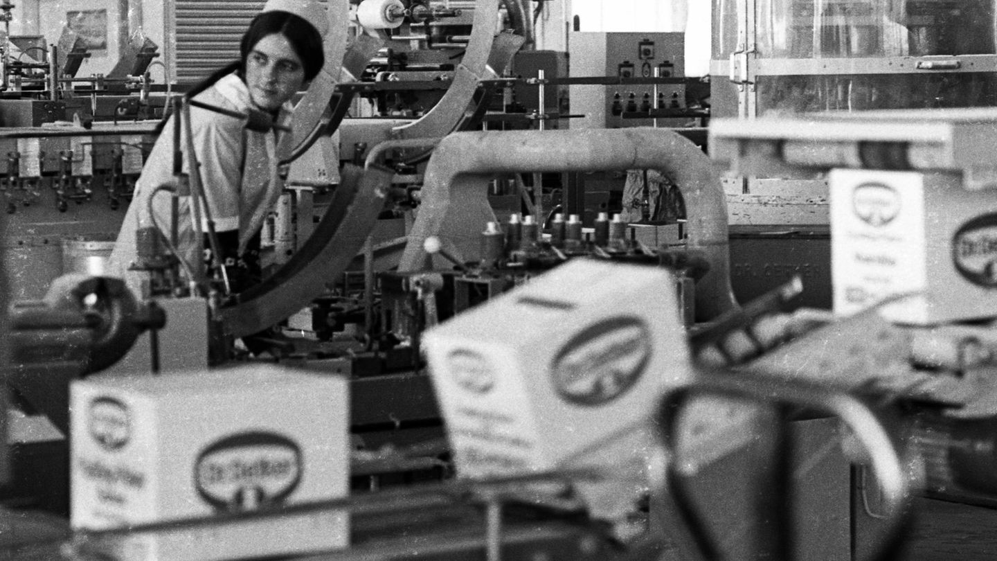 Ein Schwarzweiß-Foto zeigt eine junge Frau an einer Produktionsstraße von Lebensmitteln